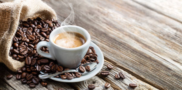 A steaming cup of coffee next to a spilled burlap sack of coffee beans.